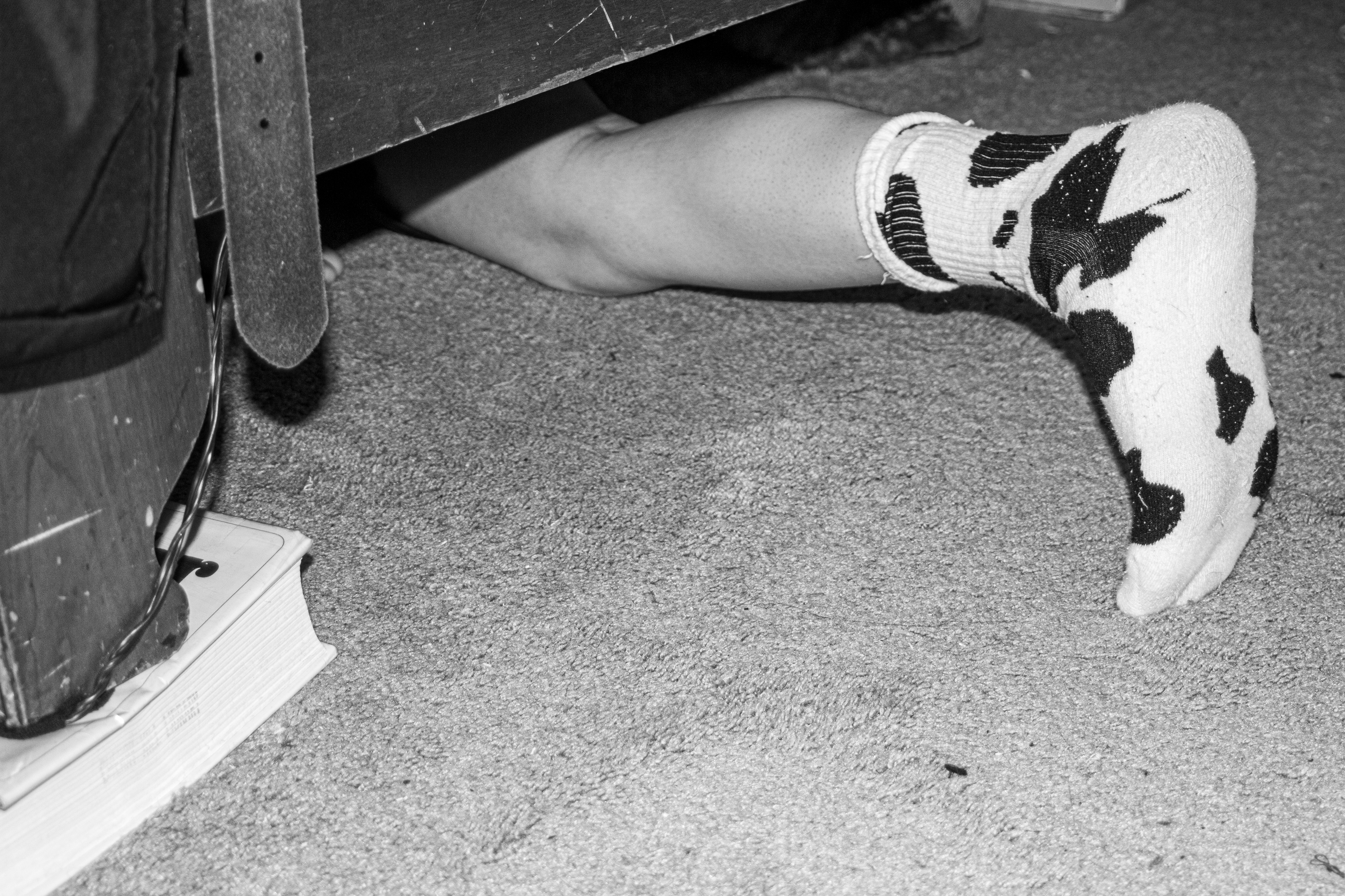 A foot is underneath a bed wearing a sock with cow print on it. The bed has a book propping it up and a belt is visible. 