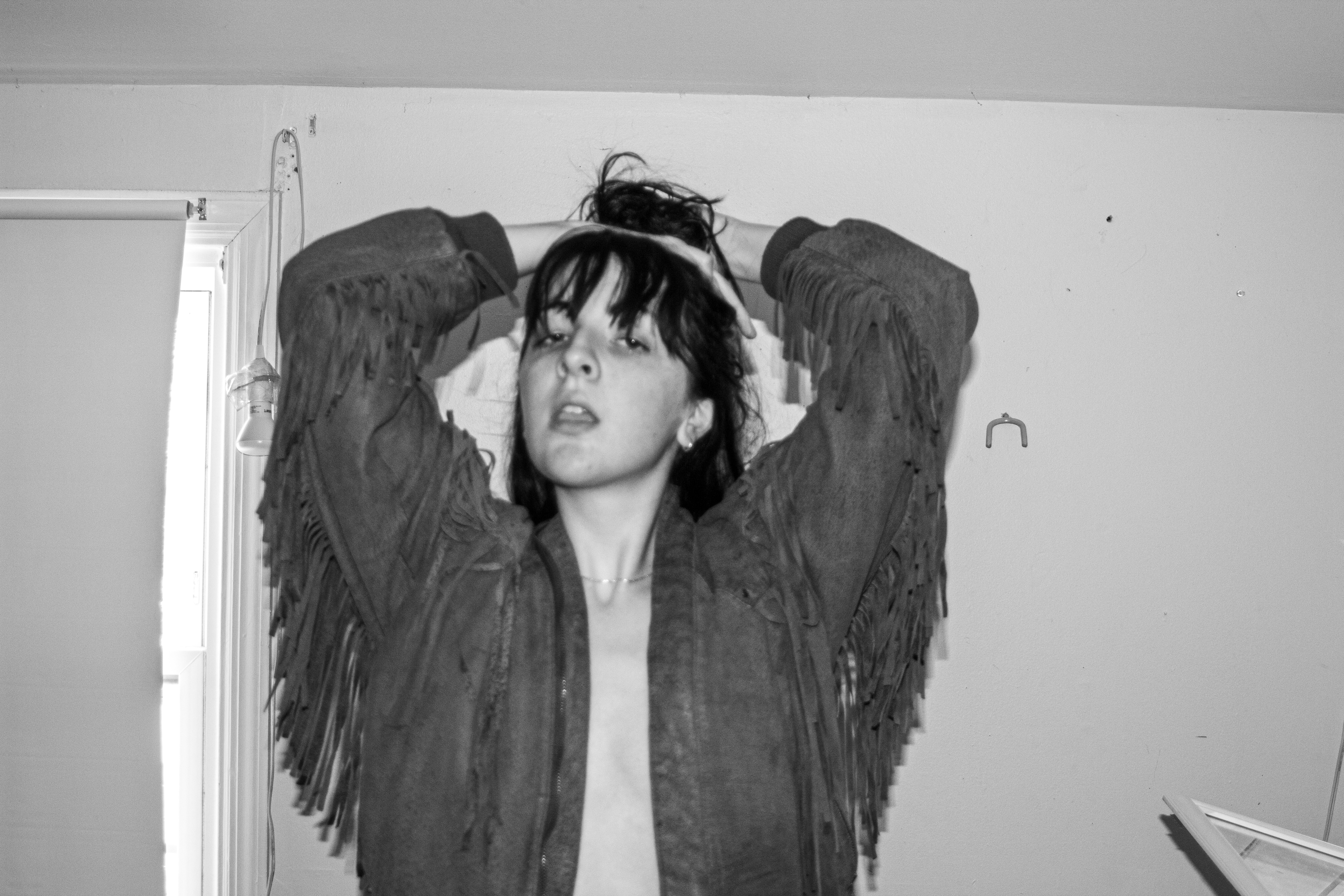 A woman is in the center of the photo holding her hair. She is wearing no shirt and a cowboy jacket with tassels in black and white