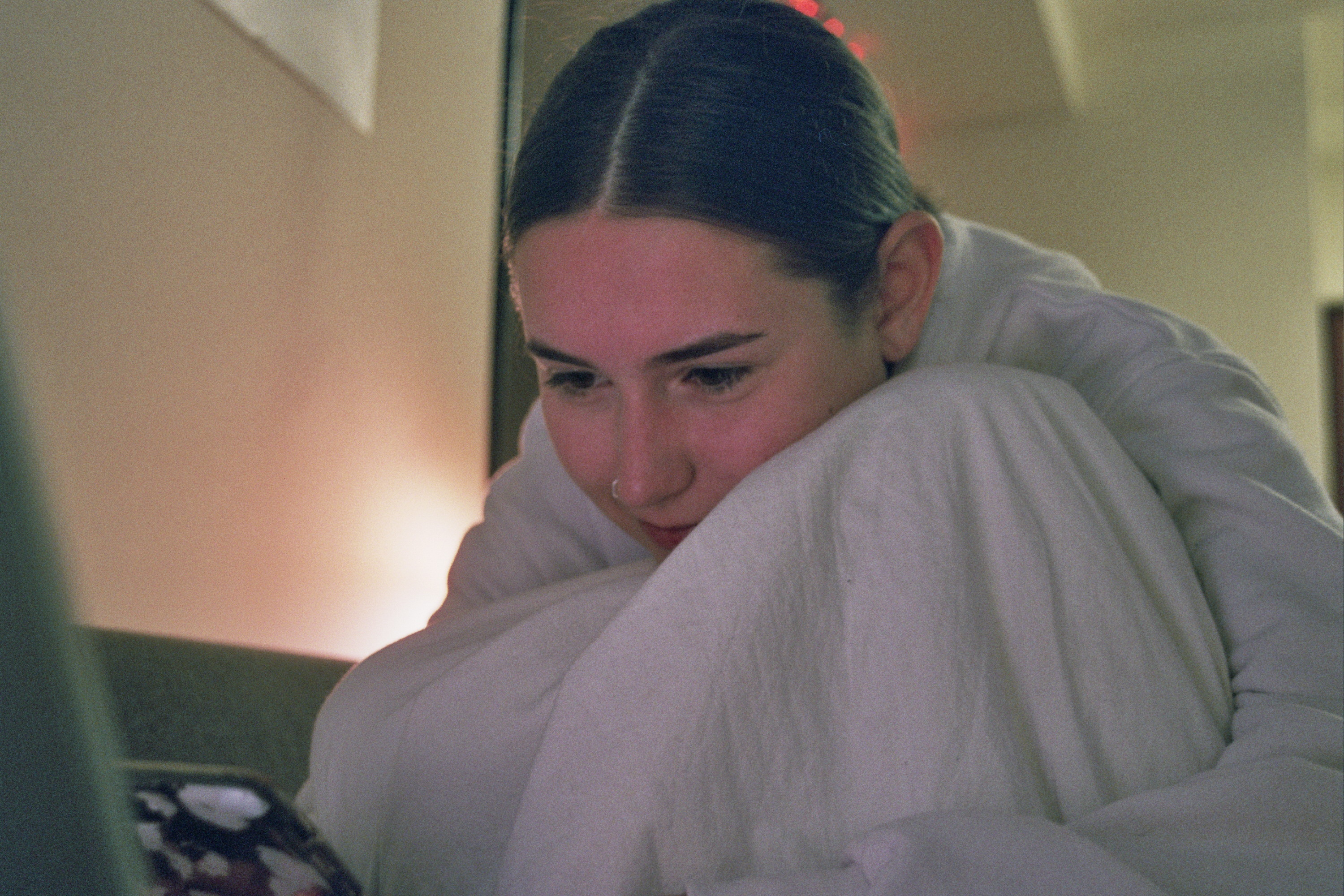 A woman is wrapped in a blanket and is looking at a laptop screen and smiling. There is a yellow hue behind her.
