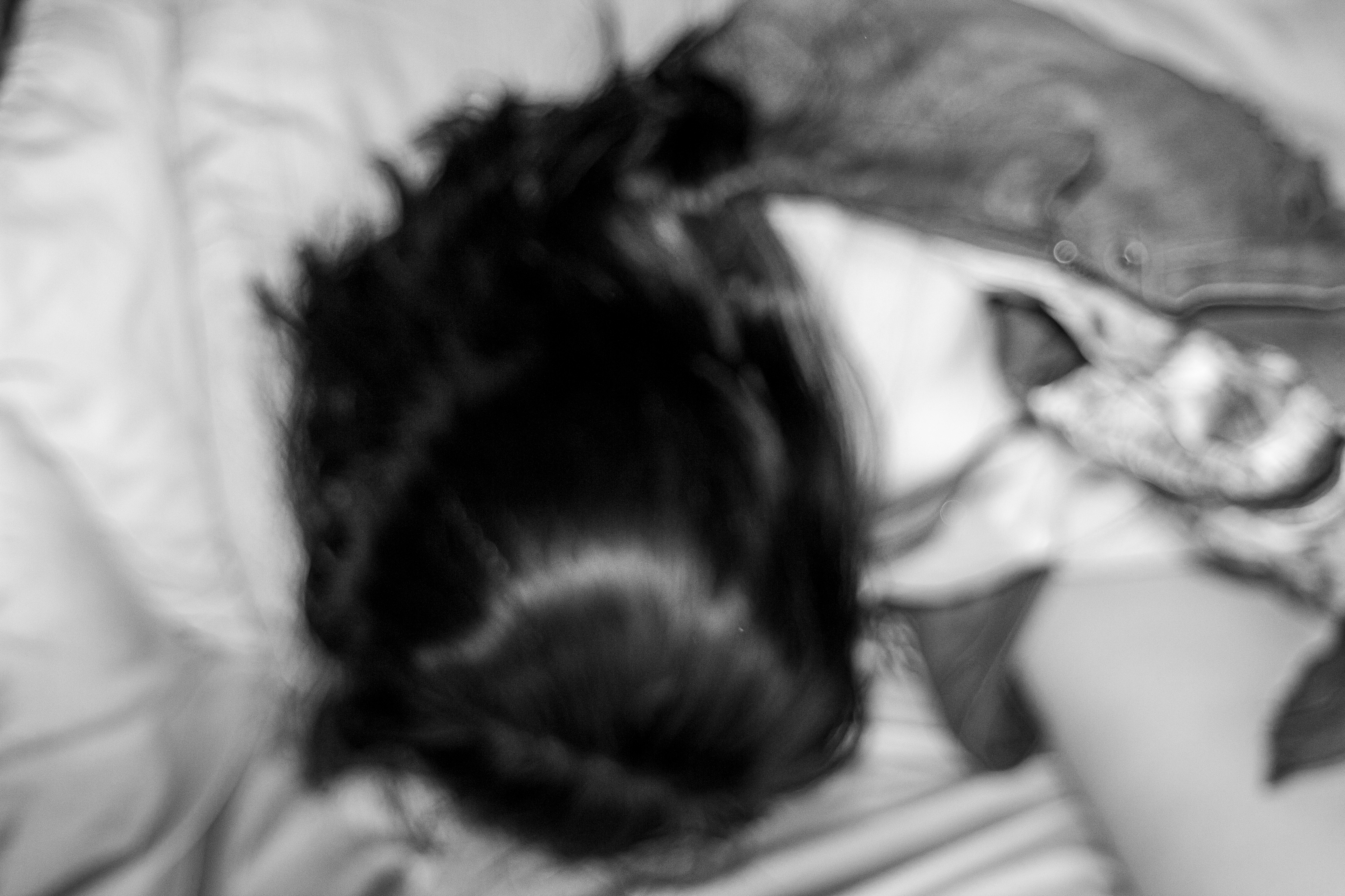 A shot from a woman above on a bed. The photo is blurry, in black and white and she is not looking at the camera.