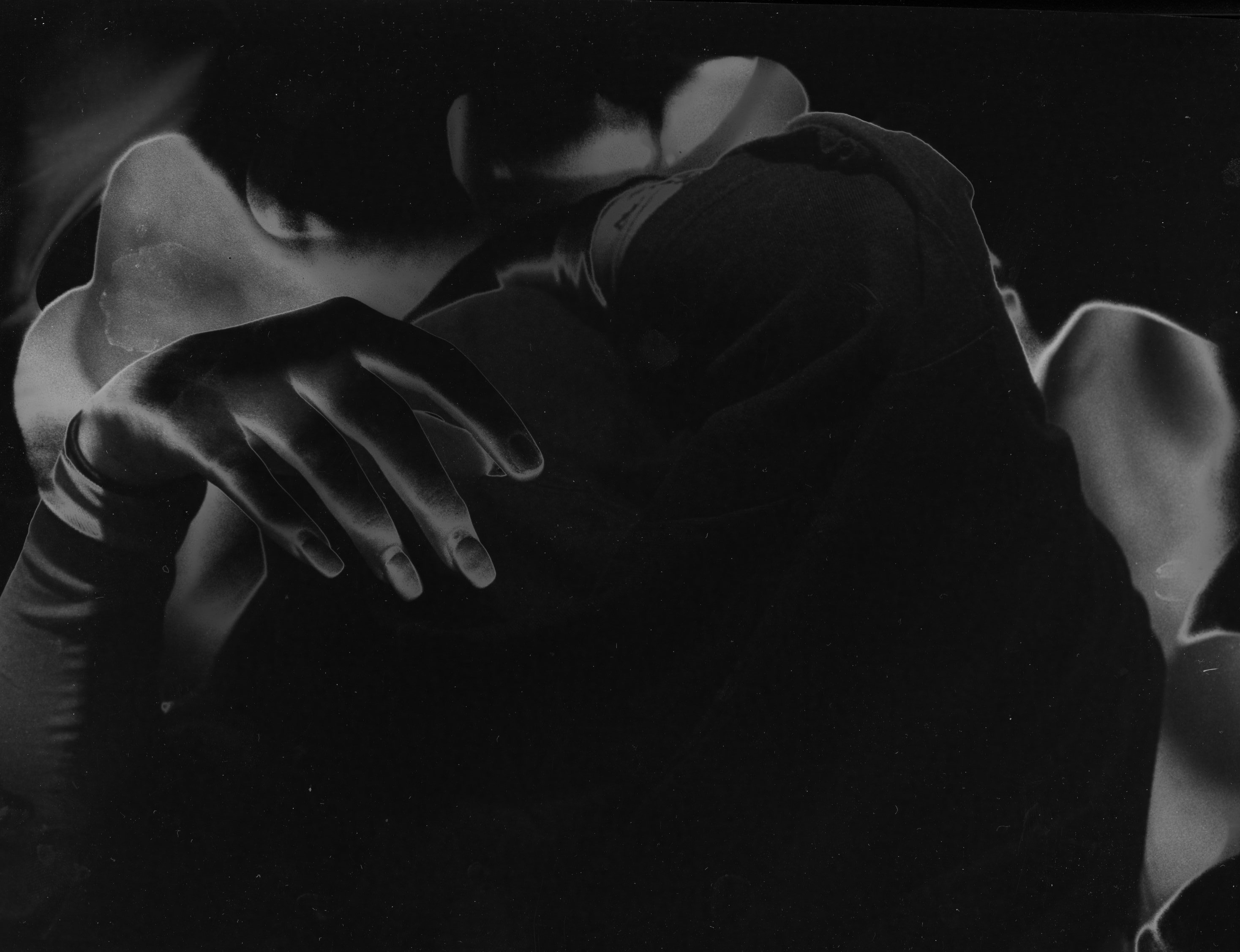A person is taking off their shirt but you can only see the black shirt and the hands. There is a strange organic shape in the background and the image is in black and white and solarized.