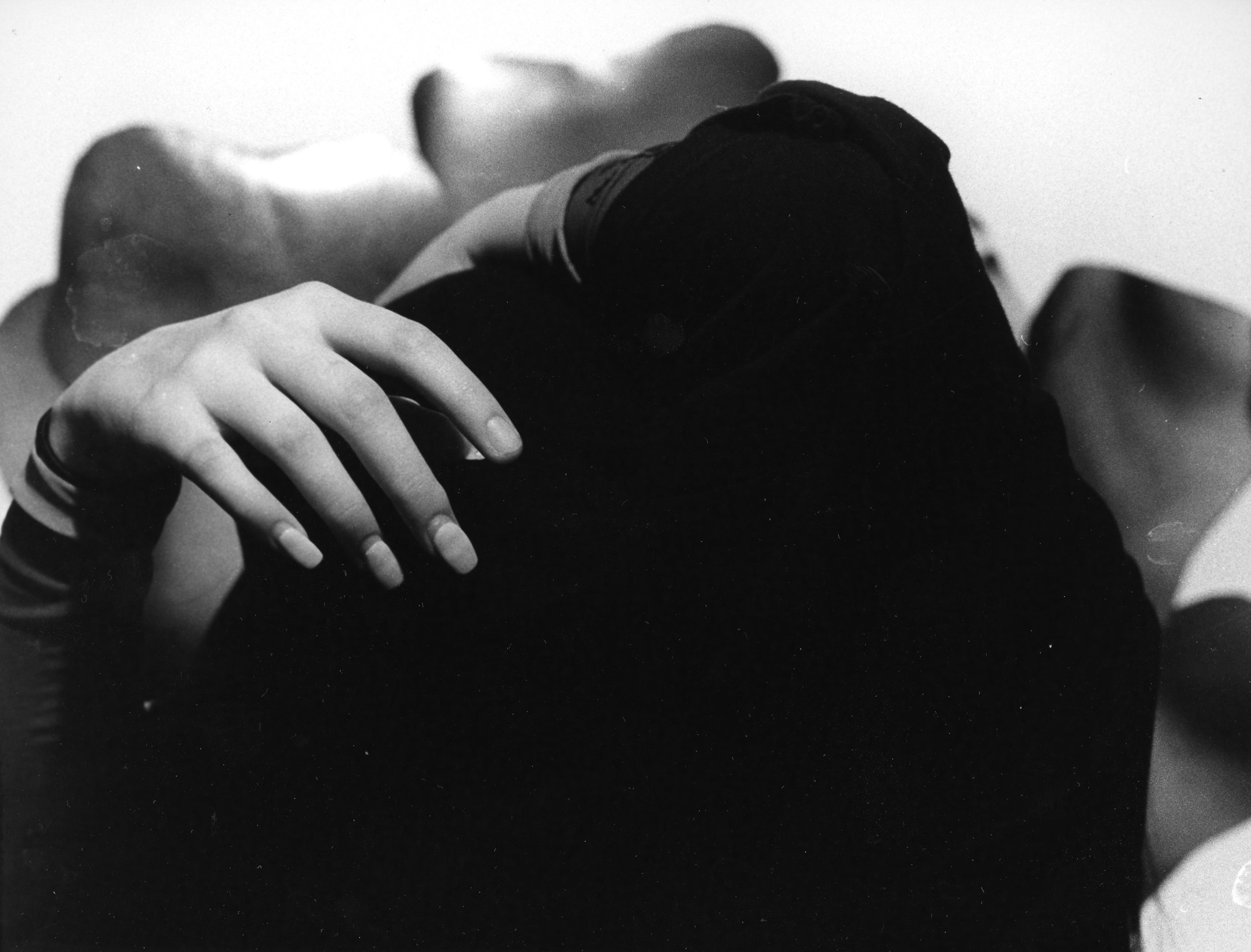 A person is taking off their shirt but you can only see the black shirt and the hands. There is a strange organic shape in the background and the image is in black and white.
