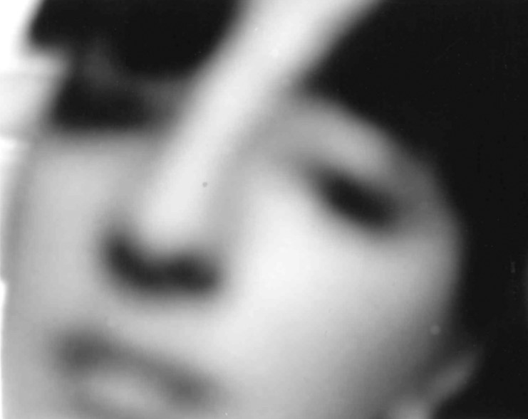 A zoomed in image of a girl's face. It is blurry and in black and white and she has bangs.