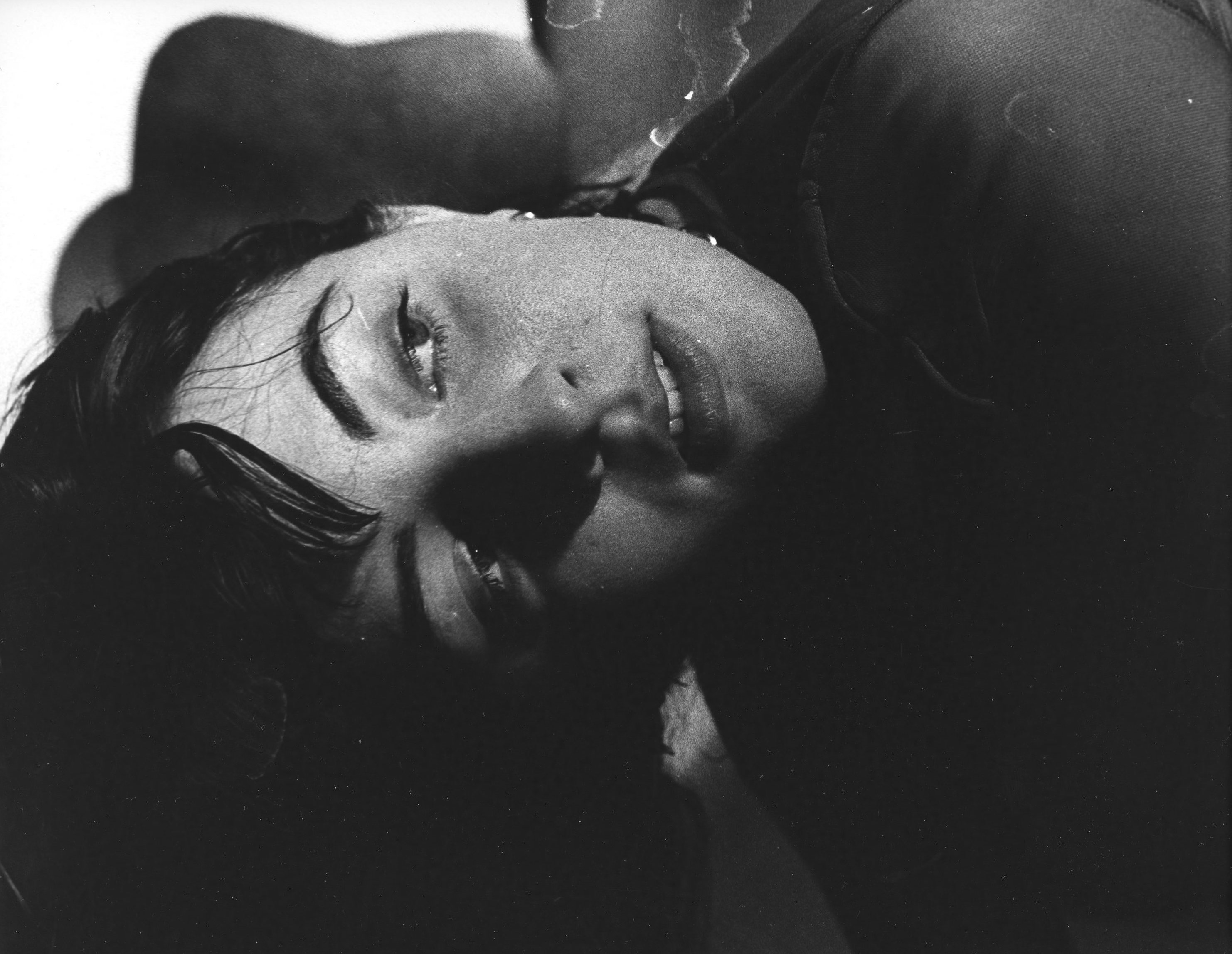 A picture of a woman bent over in black and white. You can only see her face and a strange organic background in the back and the photo is moderately to very close on the face.