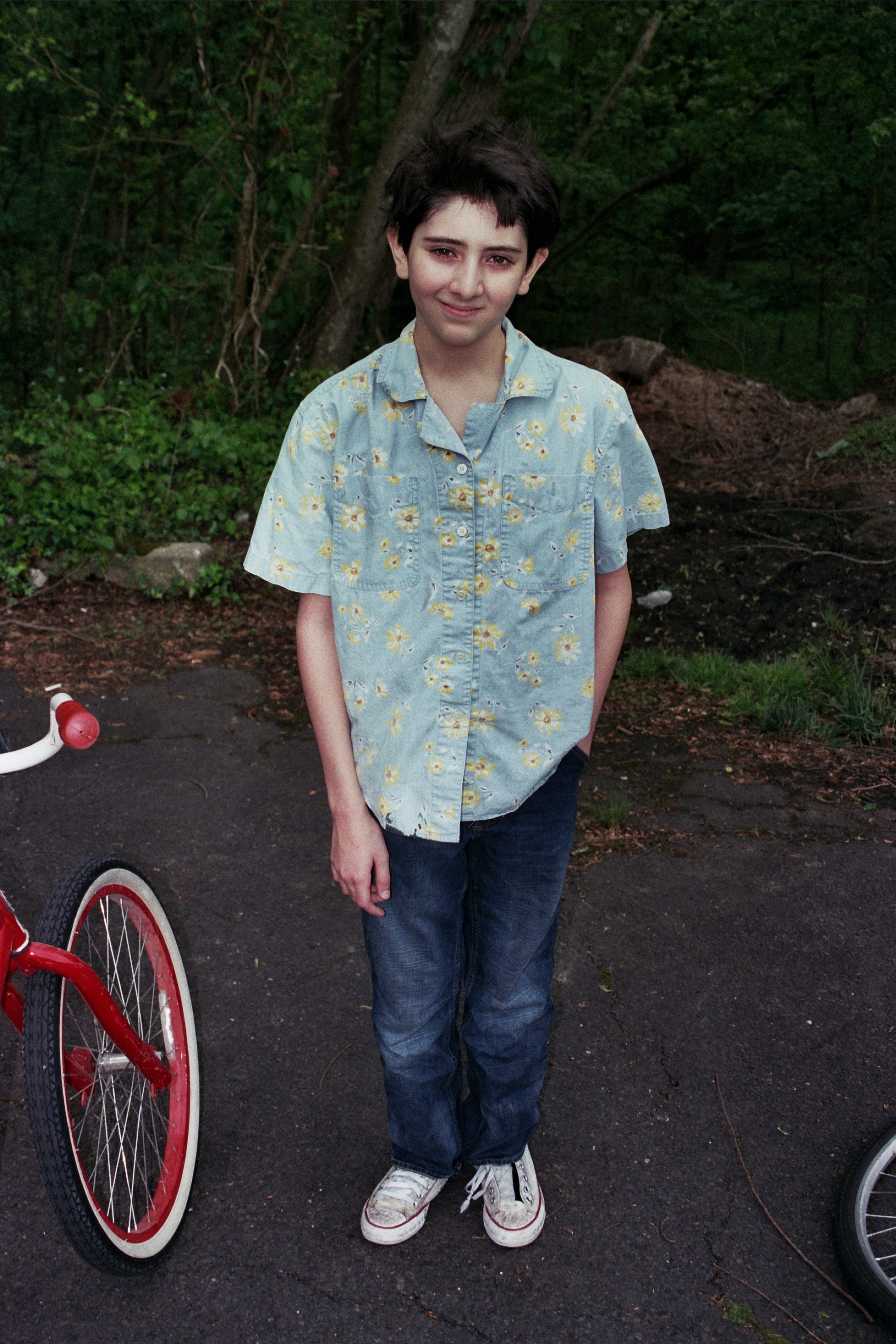 A young man looks directly into the camera. Ther is a bike behind him and his one hand is in his pocket