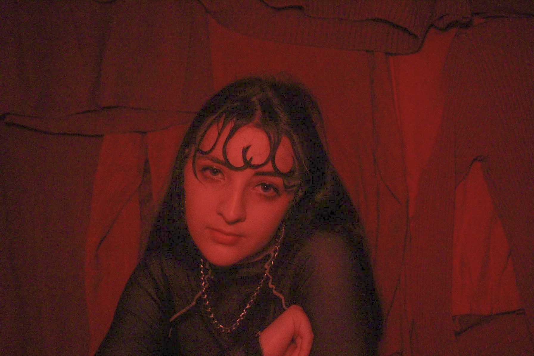 A woman all in red looks directly at the camera with her head down..