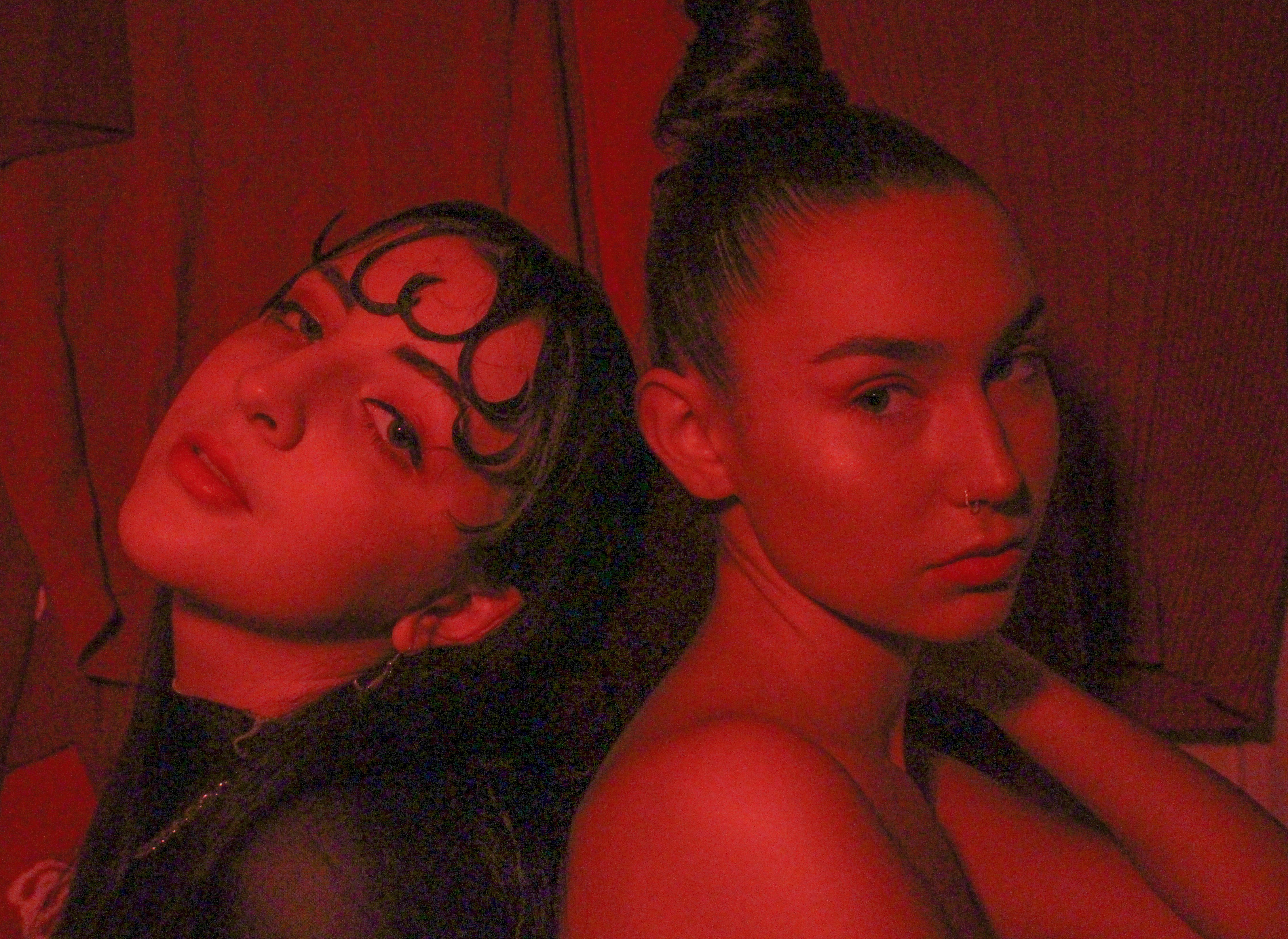 Two women in red back to back looking directly at the camera.